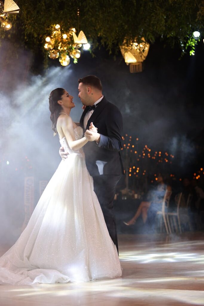 A beautifully dressed couple shares a romantic first dance at their wedding reception, surrounded by elegant decor.