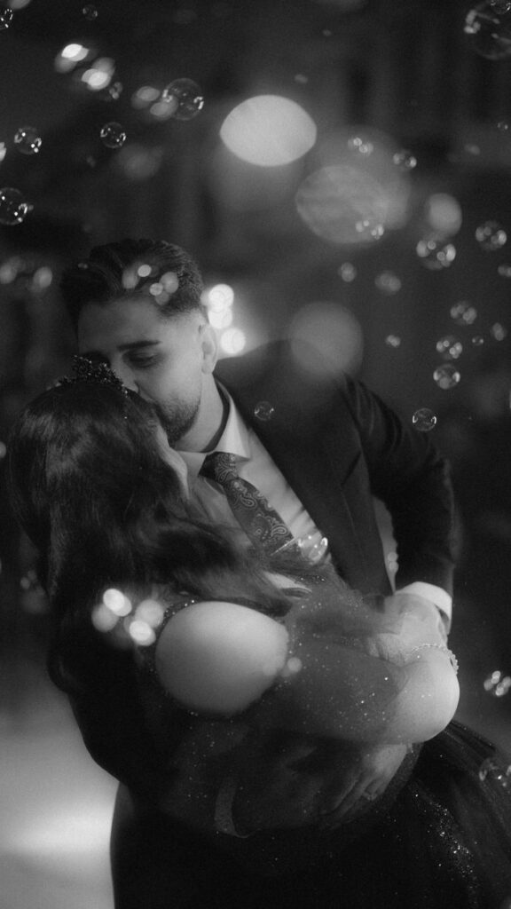 A couple shares a romantic dance amidst floating bubbles, captured in a dreamy black and white aesthetic.